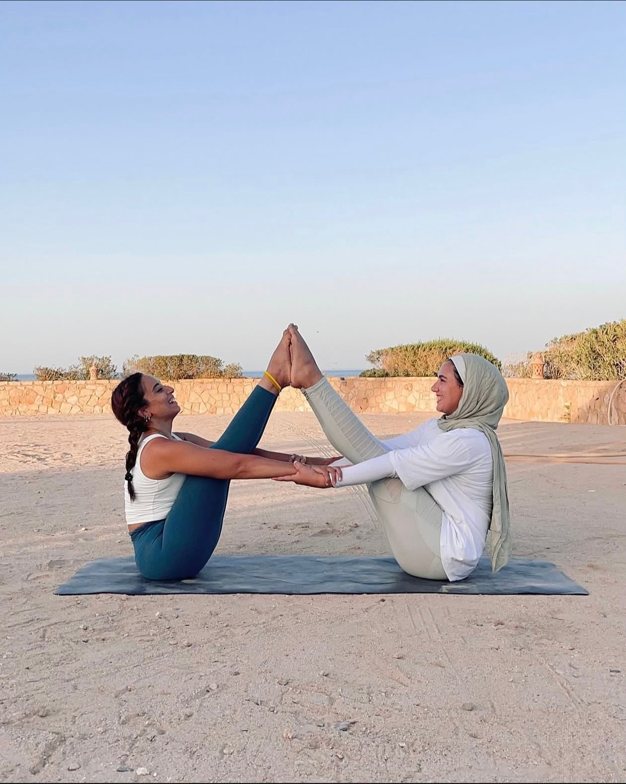 Two GND Club members doing a partner yoga pose on the beach